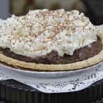 A pie with dark filling covered with fluffy white topping and shavings of chocolate