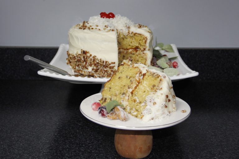 A giant slice of cake covered with a thick layer of frosting. The rest of the cake is displayed on a separate platter in the background