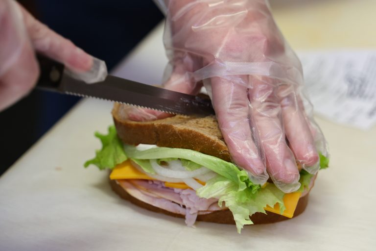 Hands preparing a deli sandwich with lettuce, tomato, and sliced meat